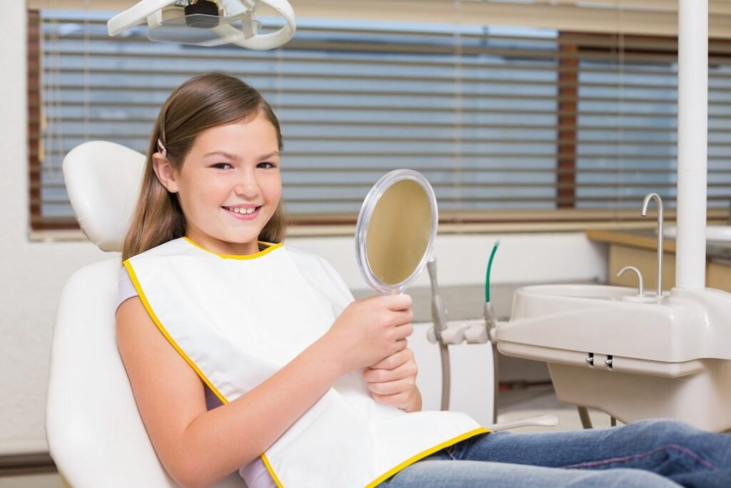 Little girl holding mirror in dentists chair at the dental clinic
